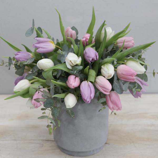 Pastel pink, lavender, and white tulips arranged loosely in a gray pot