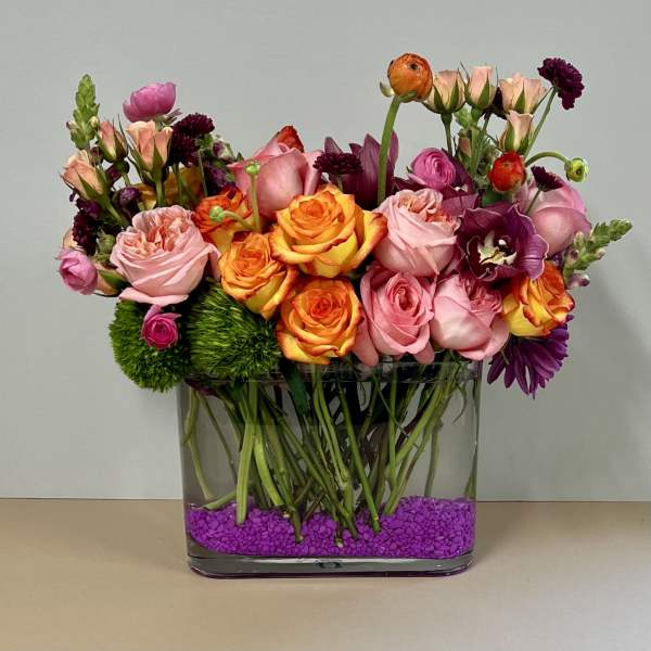 Mixed pink, orange, and purple flowers in a clear square vase