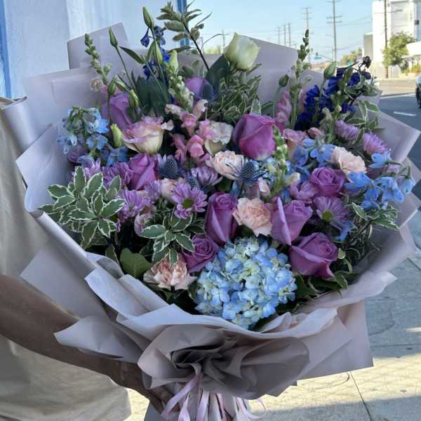 Large bouquet of purple, blue, and pink flowers wrapped in pale paper