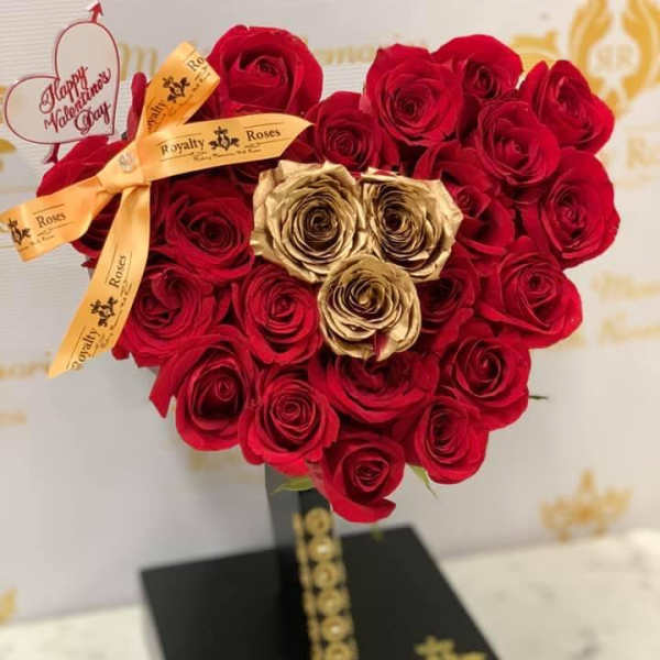 Heart-shaped rose arrangement with a gold ribbon on a black stand