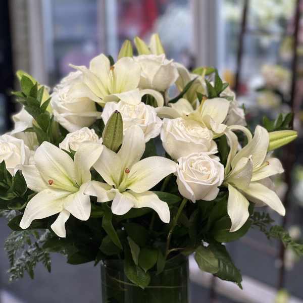 White lilies and roses arranged in a clear glass vase