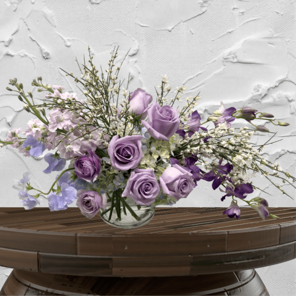 Lavender roses and purple flowers in a clear glass vase
