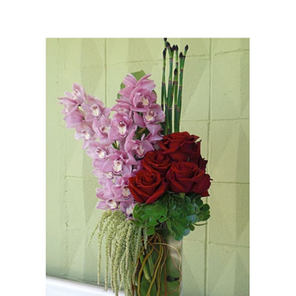 Tall arrangement of pink orchids and red roses in a glass vase