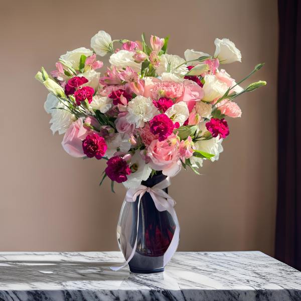 Pink and white mixed bouquet in a dark glass vase with a ribbon