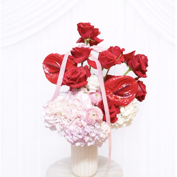Red roses and pale pink flowers arranged in a vase with ribbon