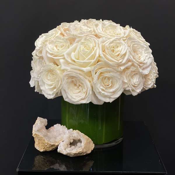 White rose bouquet in a green glass vase with two crystal rocks in front
