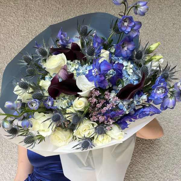 Large bouquet of blue, white, and burgundy flowers wrapped in white paper