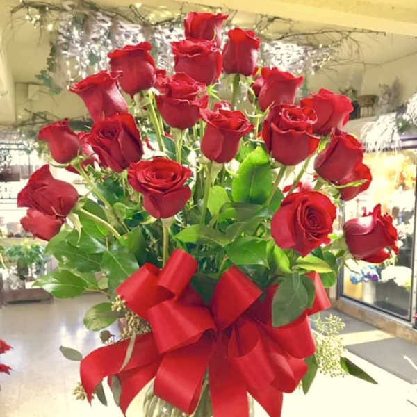 Tall bouquet of red roses in a glass vase with a large red ribbon