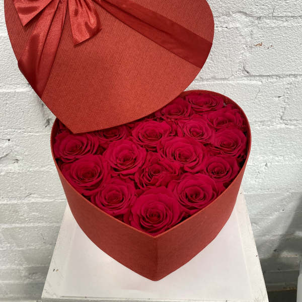 Heart-shaped box filled with red roses and topped with a red ribbon bow