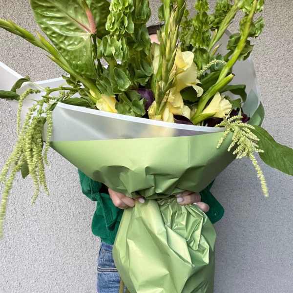 Large green bouquet with pale yellow flowers wrapped in green paper