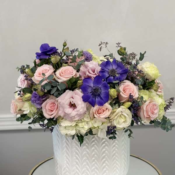 Mixed pink and purple flowers arranged in a white textured vase