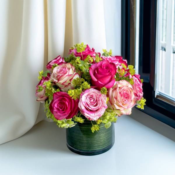 Pink and white roses arranged in a green glass vase