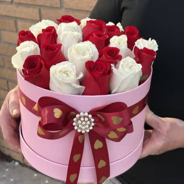 Red and white roses in a pink round box with a red ribbon