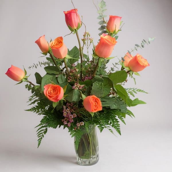 Orange roses arranged in a clear glass vase with greenery