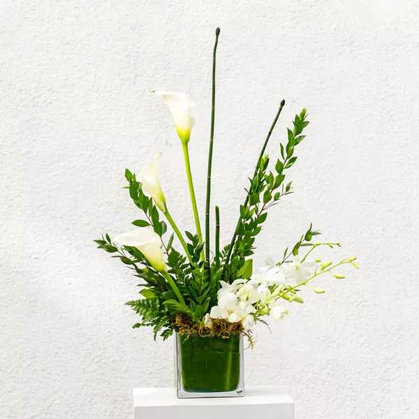 White calla lilies and orchids in a green glass vase