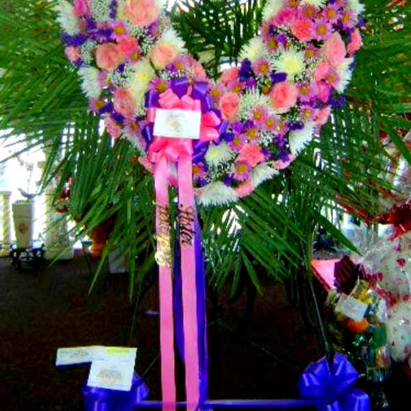 Heart-shaped floral wreath with pink, white, and purple flowers on a stand