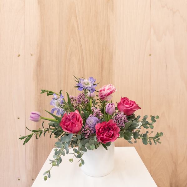 Low arrangement of pink roses and purple tulips in a white vase on a white stand
