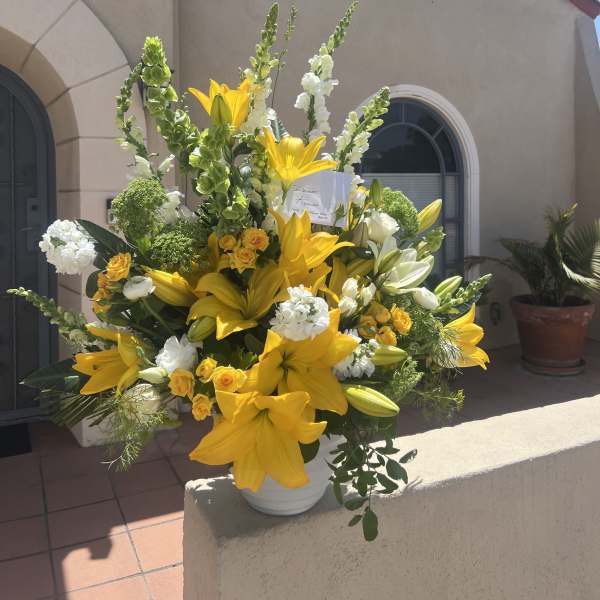 Large yellow lily and white floral arrangement in a white vase