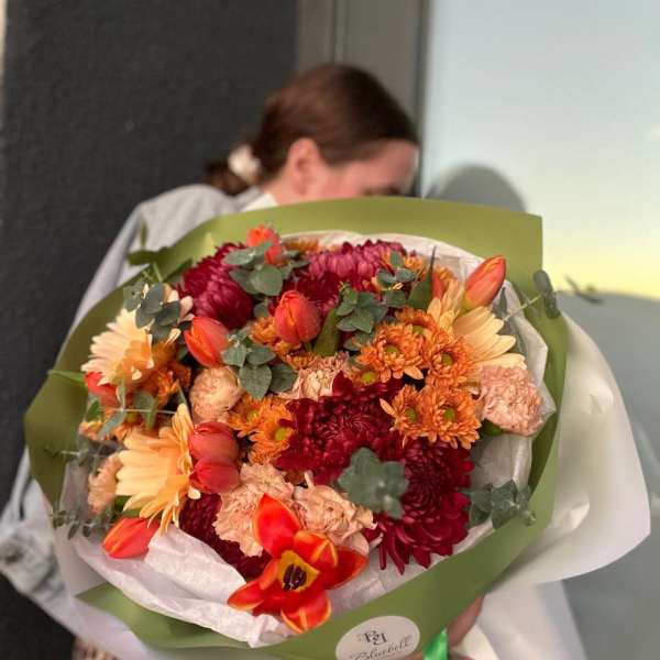 Bouquet of orange, peach, and burgundy flowers wrapped in green paper