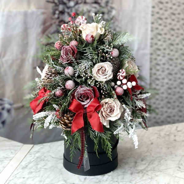 Christmas arrangement with roses, pinecones, and red ribbons in a black box