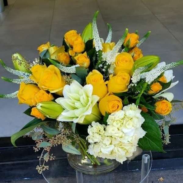 Yellow rose and white lily arrangement with white hydrangeas in a clear glass vase
