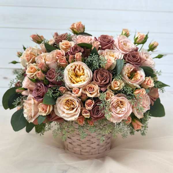 Basket arrangement of blush and mauve roses with greenery