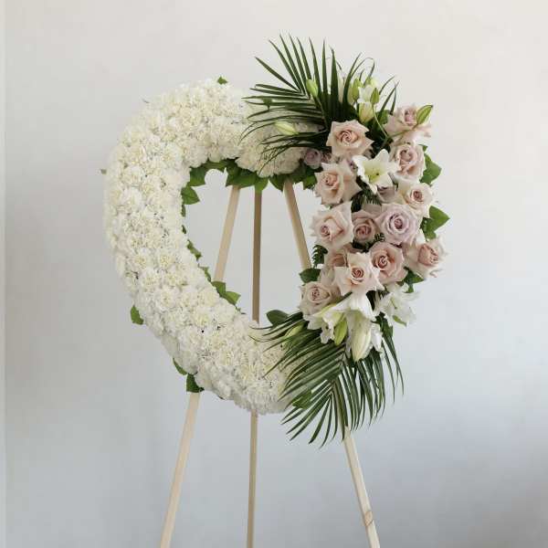 Heart-shaped white floral wreath on a stand with pale roses and lilies