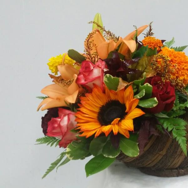 Mixed bouquet in a woven horn-shaped container with a sunflower and roses