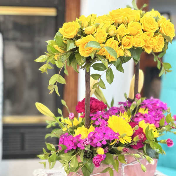 Two-tier floral arrangement with yellow roses and pink flowers in a pink box