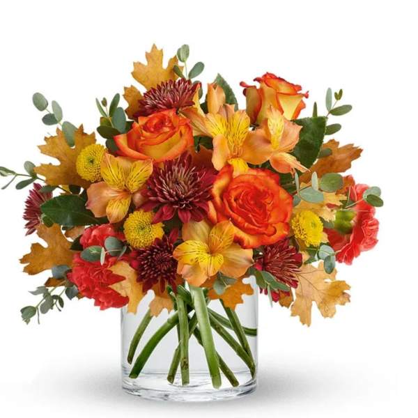 Autumn bouquet of orange roses and mixed flowers in a clear glass vase