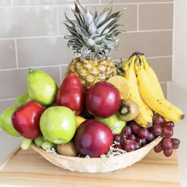 Basket of assorted fruit with pineapple, bananas, grapes, apples, and kiwi