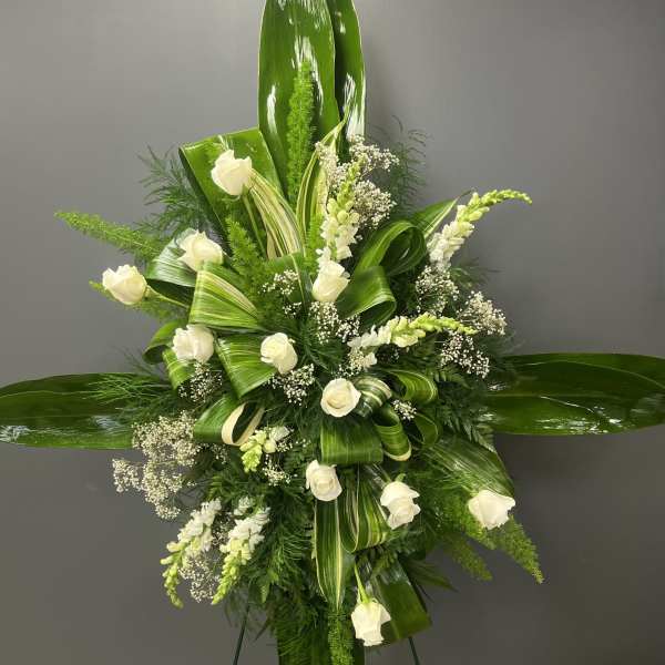 White roses and small white blooms arranged with glossy green leaves on a standing easel.