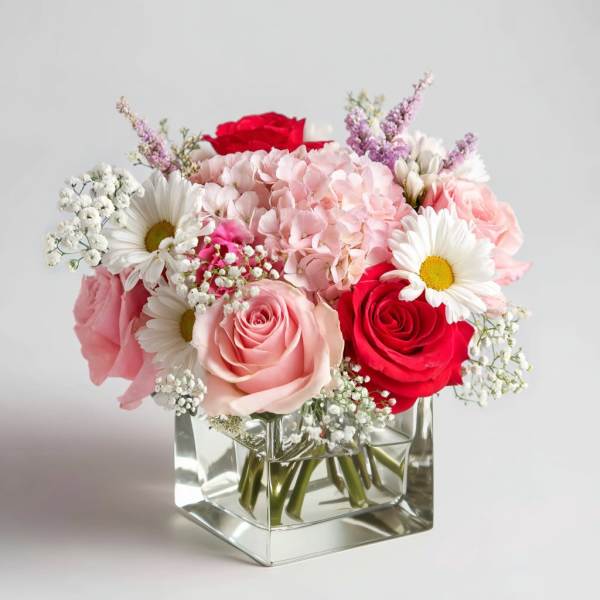 Pink and red roses with daisies in a clear glass vase