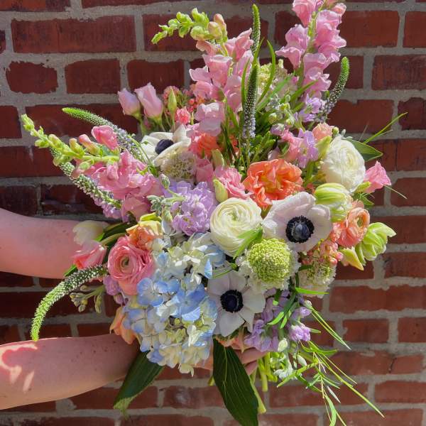 Handheld bouquet of pastel pink, white, blue, and peach flowers