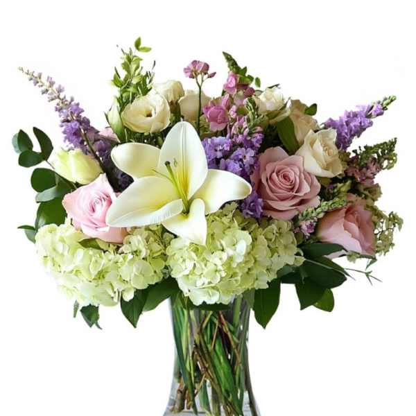 Bouquet of white lilies, pink and cream roses, and purple flowers in a glass vase