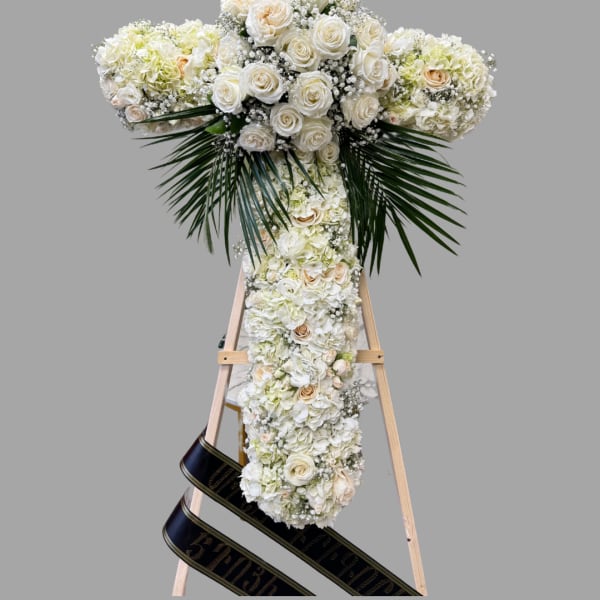 White floral cross on a wooden easel with black ribbon