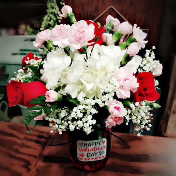 Bouquet of red roses, pink carnations, and white hydrangea in a vase