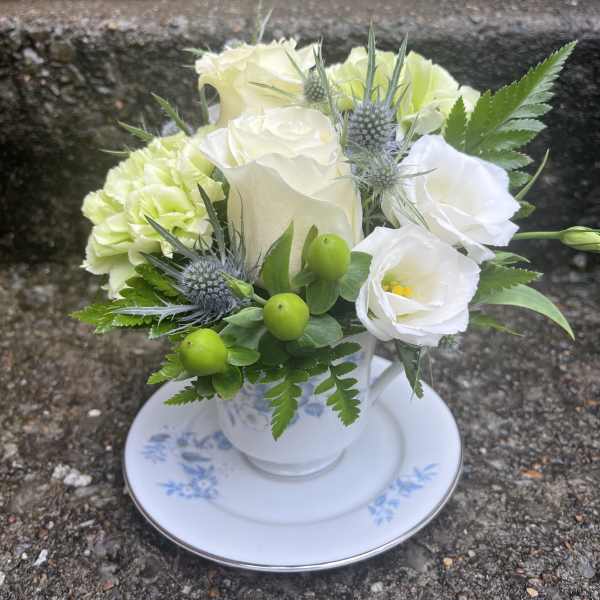 White and pale green floral arrangement in a teacup on a saucer