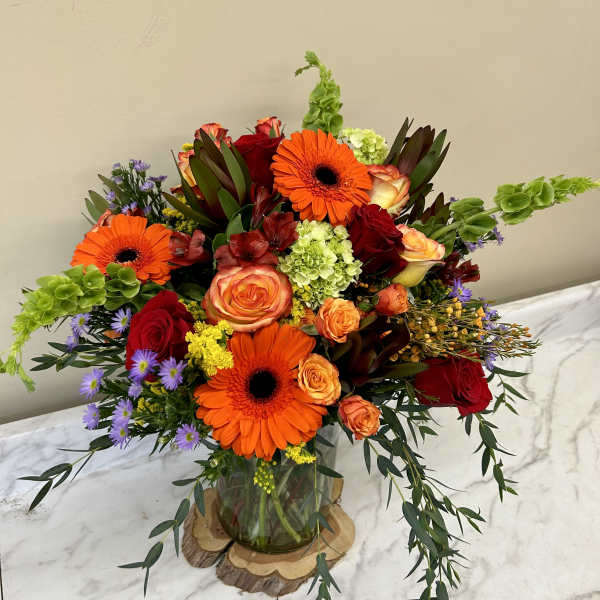 Bright mixed bouquet with orange gerbera daisies and red roses in a glass vase