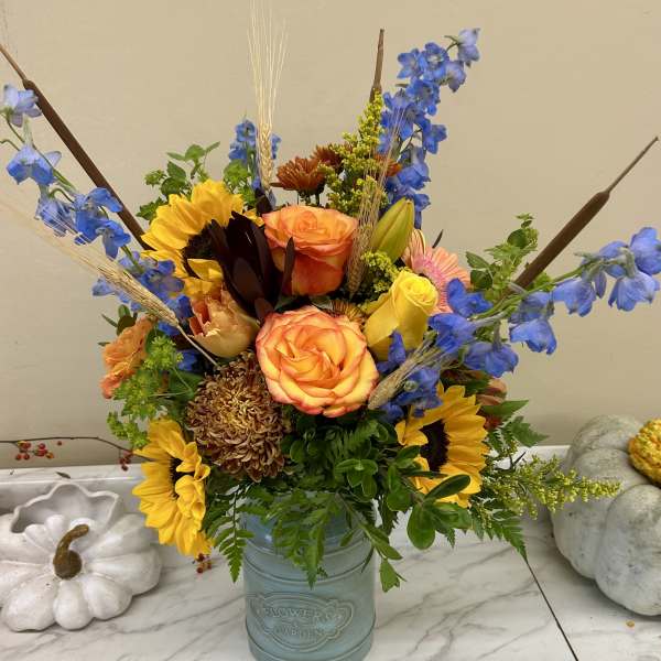 Mixed bouquet in a blue vase with sunflowers, roses, and blue delphinium