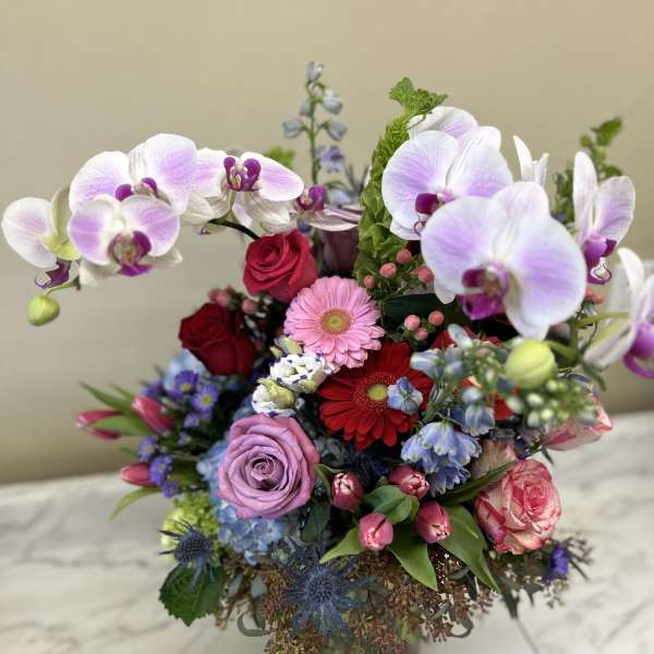 Mixed bouquet with orchids, roses, gerbera daisies, and tulips in a glass vase