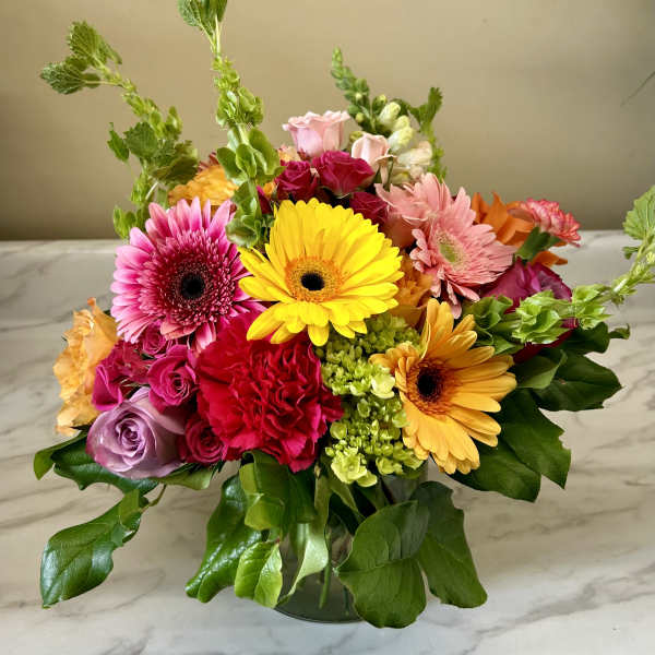 Mixed bouquet of gerbera daisies, roses, and carnations in a glass vase