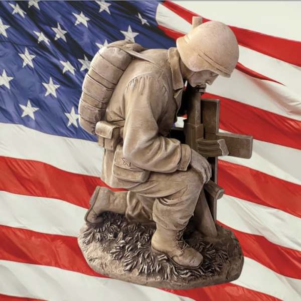 A kneeling soldier statue in front of an American flag.