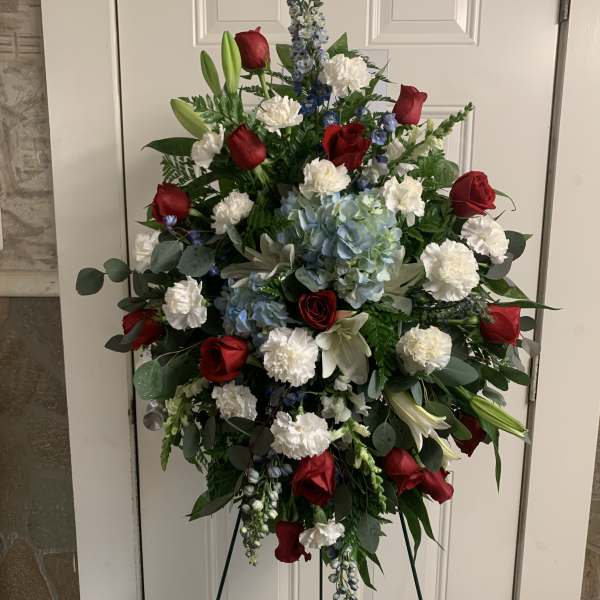 Standing floral spray with red roses, white carnations, and blue flowers