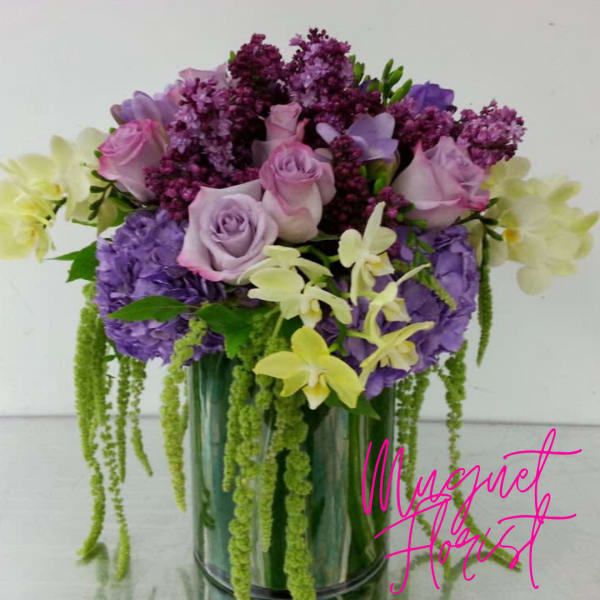 Lavender roses and purple flowers in a glass vase with trailing green accents