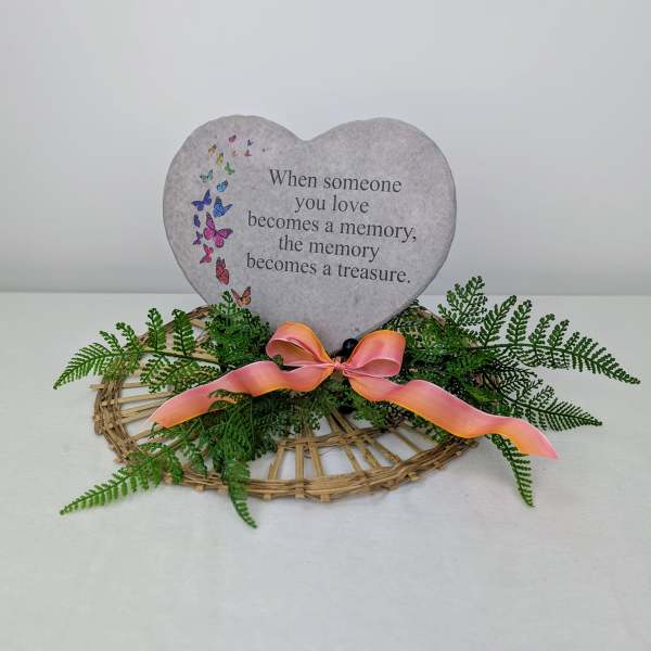 Heart-shaped memorial sign with greenery and a pink ribbon on a wicker base