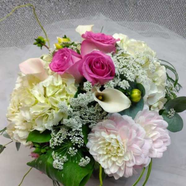 Pink roses and pale blooms arranged with white calla lilies in a bouquet