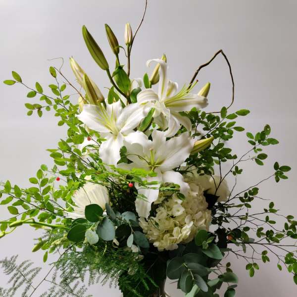 White lilies and hydrangea in a glass vase with airy greenery