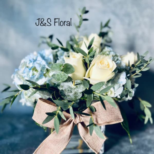 White roses and blue hydrangeas in a glass vase with a burlap bow