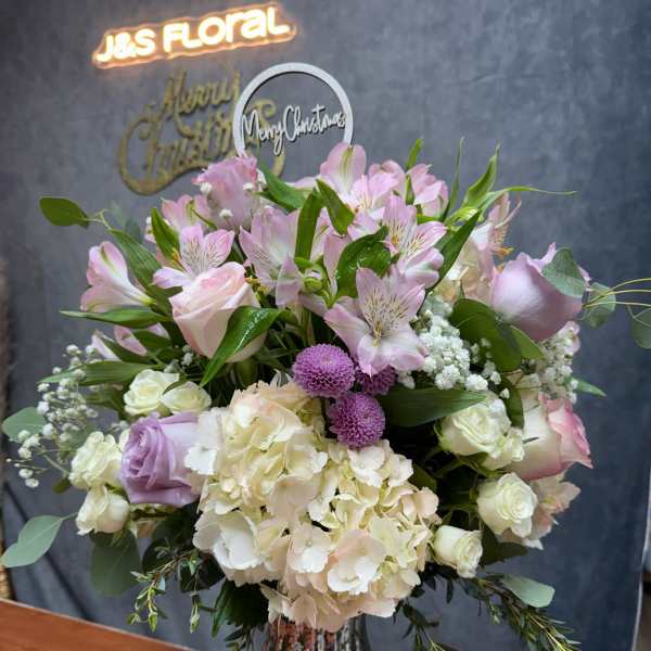 Pink and white floral arrangement in a glass vase with a Christmas topper